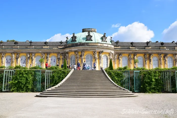 Frontalansicht der Gartenfassade von Schloss Sanssouci mit zentraler Freitreppe, Kuppel und Besuchern.